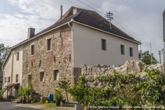 Ansicht der Kirche Arbing mit dem Mauerprojekt nach Entwürfen von Gottfried Kranzl. An die Dorfmauer schließt sich noch ein Gebäude mit unverputzter Südseite an, die auf das hohe Alter hinweist.