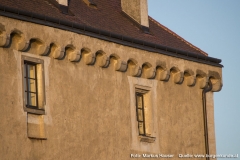 Direkt unter dem Walmdach ein umlaufender Stichbogenfries auf Kragsteinen. Beim linken Fenster ist unterhalb eine Vertiefung in der Mauer zu erkennen. Für welchen Zweck, bleibt unklar.