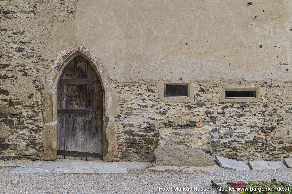 Neben der gotischen Eingangstüre in die Kapelle befinden sich noch zwei schmale, schlitzartige Öffnungen.
